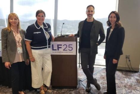 Four people stand smiling beside a podium with a sign reading “LF25: Accelerating Regenerative Action” at a conference event.
