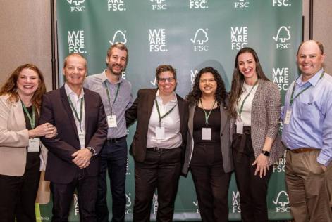 Seven people stand together smiling in front of a "We are FSC" banner.