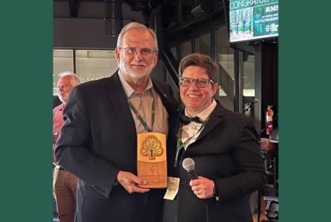 Two people smile together as one holds an FSC wooden award plaque.