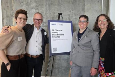 Four people stand smiling beside a sign that reads “SF Climate Week: Sustainable Finance,” posing together at an indoor event.