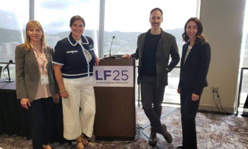 Four people stand smiling beside a podium with a sign reading “LF25: Accelerating Regenerative Action” at a conference event.