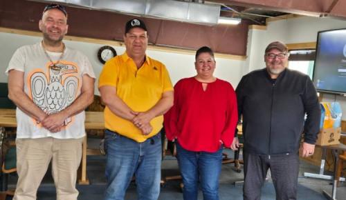 Four people stand together indoors, smiling for the camera in a meeting room.