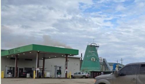 ChatGPT said:  A green-roofed gas station labeled “MTE” sits beside an industrial building with a large green cone-shaped structure marked “Menominee Tribal Enterprises” under a cloudy sky.