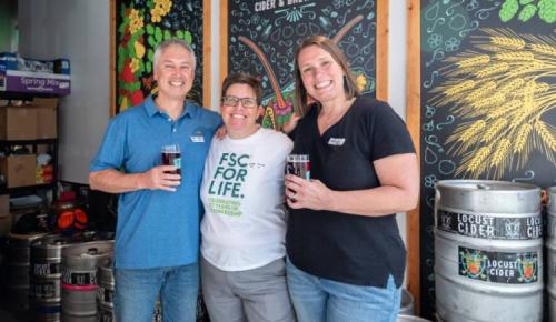 Three attendees smile together holding drinks at an FSC social event.