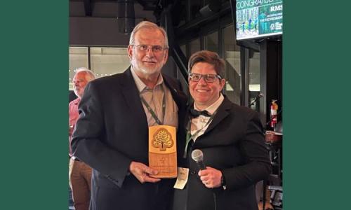 Two people smile together as one holds an FSC wooden award plaque.