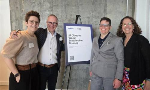 Four people stand smiling beside a sign that reads “SF Climate Week: Sustainable Finance,” posing together at an indoor event.