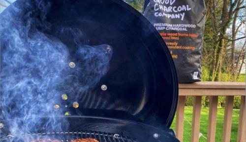 Smoke rises from a grill with a bag of The Good Charcoal nearby.