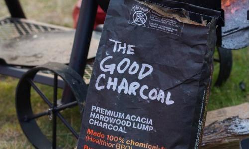 Bag of The Good Charcoal placed near a grill outdoors.