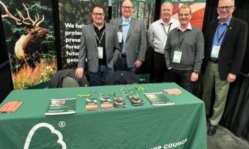 Five people stand behind an FSC display table at a conference booth promoting sustainable forestry.