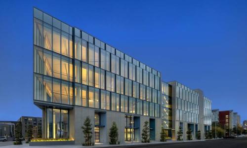 Wide-angle view of glass building glowing against the evening sky.