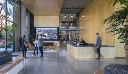 Modern office lobby with wood accents and people conversing near a reception desk.