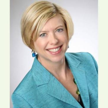 A professional headshot of a woman wearing a turquoise blazer, smiling against a neutral studio background.